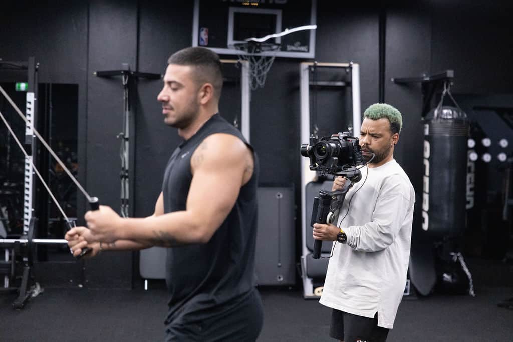 Man filming another man exercising at the gym.