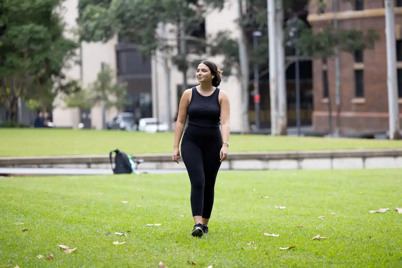 Woman walks in city park on green lawn.